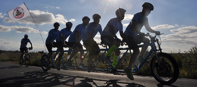 The six-man TanDam tandem in silhouette, with a support rider alongside