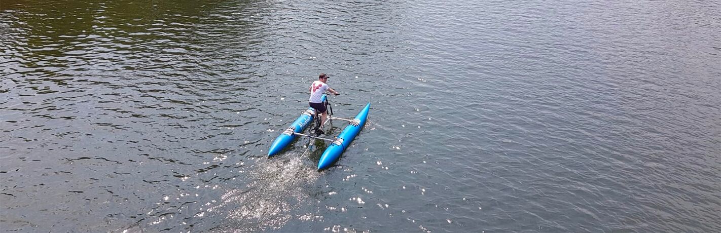A rider on a bike fixed to a twin-float water craft, crossing open water